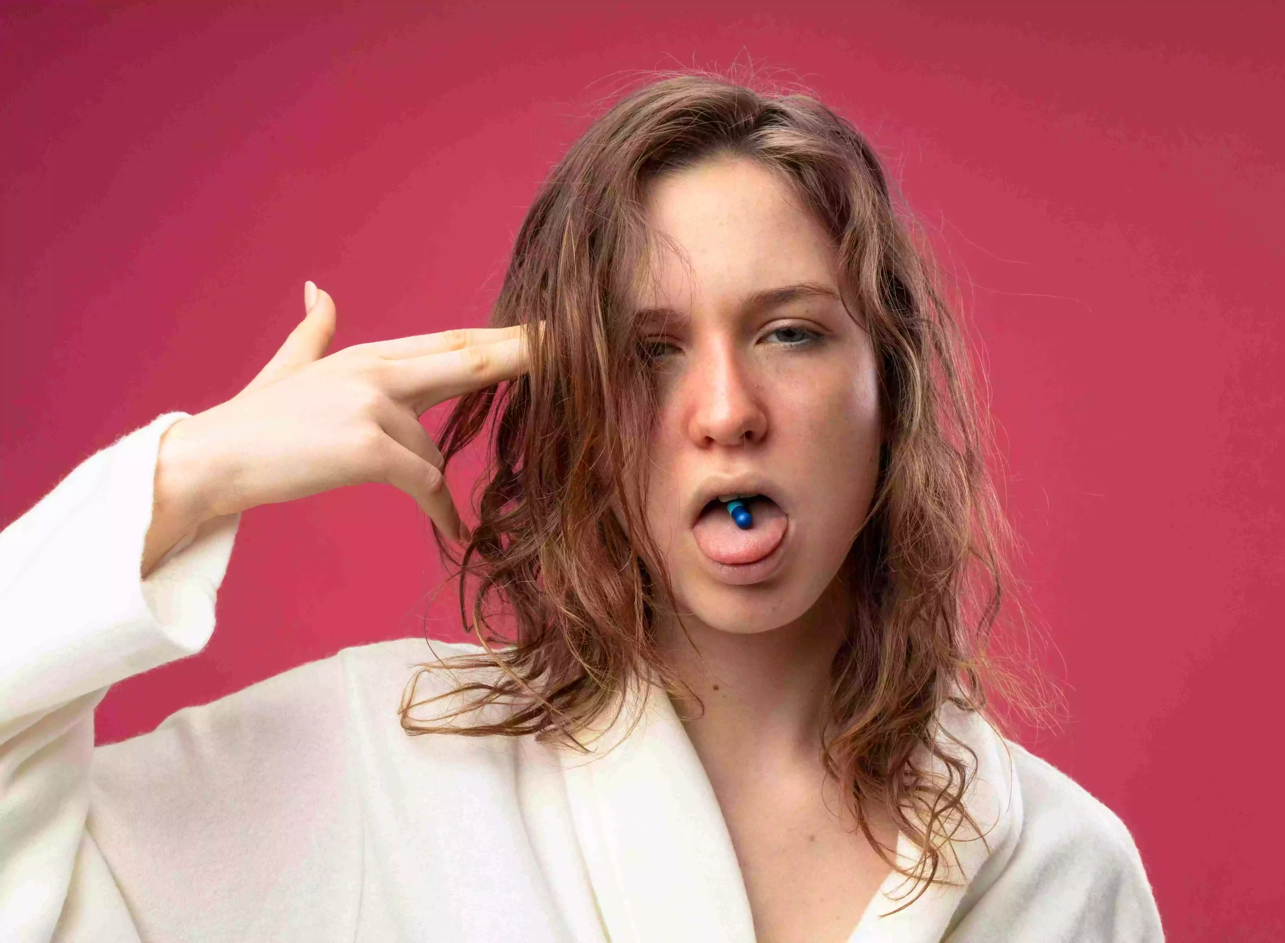 weak-young-ill-girl-wearing-white-robe-putting-pill-mouth-showing-pistol-gesture-isolated-pink a